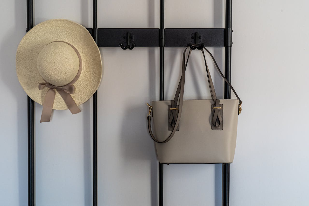 A stylish sun hat and leather handbag hanging on a modern wall hook indoors.